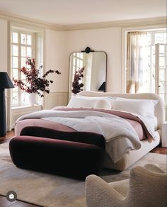 a large bed sitting in a bedroom on top of a hard wood floor next to two windows