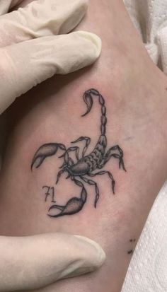 a scorpion tattoo on the left ankle and right leg is shown in black ink, while someone's hands are holding it