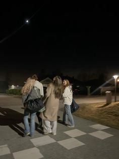 three women walking down the street at night with their backs turned to the camera,