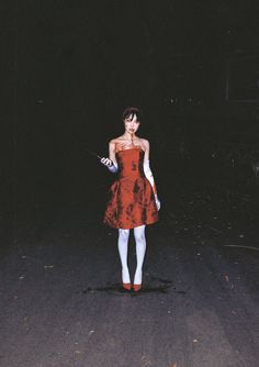 a woman in a red dress and white stockings is walking down the street at night