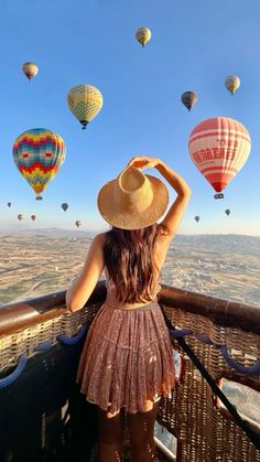 a woman in a straw hat looking out over the hot air balloons flying above her