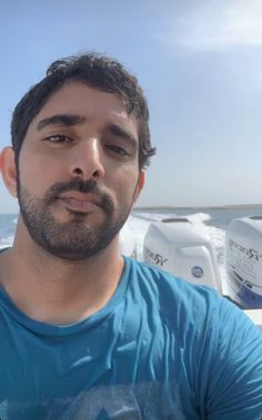 a man in a blue shirt standing next to the ocean and looking at the camera