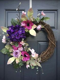 a wreath with purple flowers and greenery hanging on a front door, ready to be hung