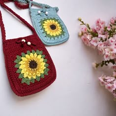 two crocheted purses sitting on top of a table next to pink flowers