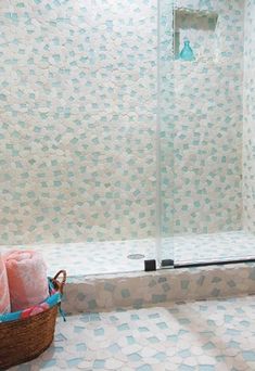 there is a basket with towels on the floor in front of a shower stall that has blue and white wallpaper