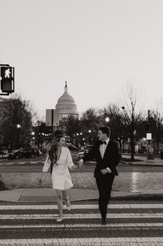 a man and woman walking across a cross walk in front of the capitol building at night