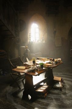 an empty table in a dark room with sunlight coming through the window and books on it