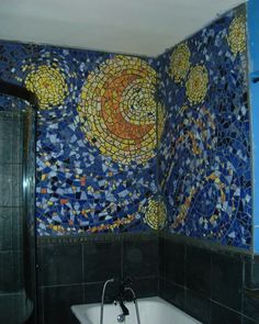 a bath tub sitting next to a bathroom wall covered in blue and yellow mosaic tiles