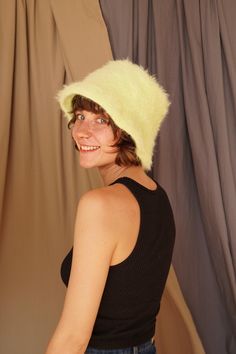 a woman wearing a black top and a yellow hat smiles at the camera while standing in front of a curtain