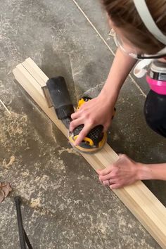 a woman using a sander on a piece of wood that is laying on the ground