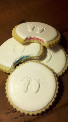 four cookies with baby footprints on them sitting on top of a wooden table next to a cupcake