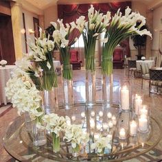 flowers and candles are arranged in vases on a glass table