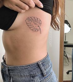 a woman's stomach with a tattoo on her side and a leaf in the middle