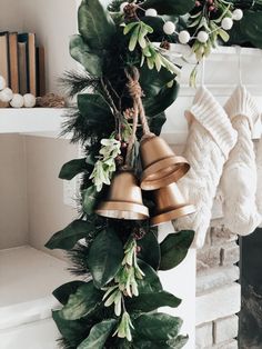 a christmas wreath with bells and greenery hanging from it's sides in front of a fireplace