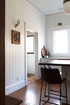 a kitchen with white walls and wood flooring next to a bar stool in front of a window