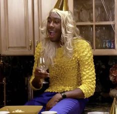 a woman sitting on the kitchen counter with a glass of wine in her hand while wearing a party hat