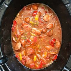 there is a stew in the crock pot with sausages, peppers and corn