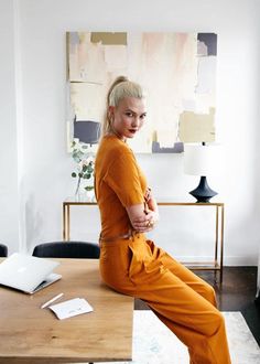 a woman in an orange jumpsuit sitting on a table with a laptop and flowers