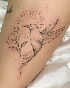 a small tattoo on the leg of a woman with a hummingbird flying over flowers