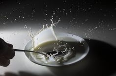 a person is spooning milk out of a bowl with water splashing on it