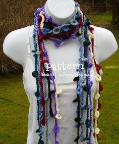 a white mannequin wearing a multicolored crocheted scarf on top of a green grass covered field