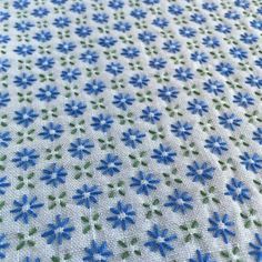 blue and green flowers on white fabric with small dots in the center, closeup