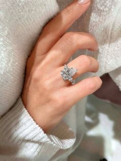 a woman's hand with a diamond ring on her left hand, wearing a white sweater