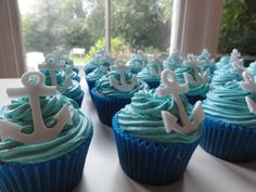 cupcakes with blue frosting and white anchors on them sitting on a table