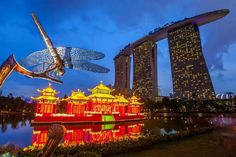 a dragon statue is in front of the water and buildings with lights on them at night