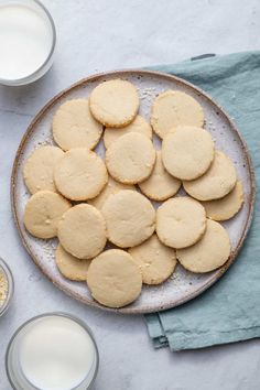 cookies and milk are on a plate next to two glasses of milk, one is empty