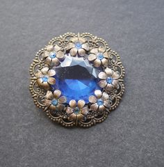 Czech style brooch, pressed filigree metal.  Large dark blue rhinestone in centre, flowers around the edge with smaller blue rhinestones. Pin and C clasp. Good condition. 5cm diameter. Vintage Blue Brooches For Jewelry Making, Vintage Sapphire Brooches For Gifts, Vintage Sapphire Brooches As Gift, Ornate Blue Brooches For Wedding, Ornate Blue Wedding Brooches, Czech Style, Vintage Brooch, Blue Rhinestones, The Edge