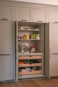 an open cabinet in the middle of a kitchen with wooden floors and white cupboards