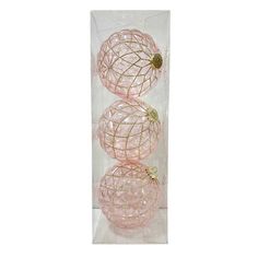 three pink glass ornaments sitting in a clear box on a white surface with gold accents