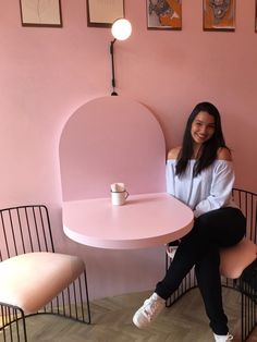 a woman sitting at a table in front of a pink wall