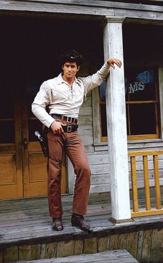 a man leaning against the side of a wooden building with his hand on the door