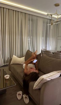 a woman laying on top of a couch in front of a window reading a book