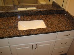 a bathroom sink with granite counter top and white cabinetry in front of the mirror