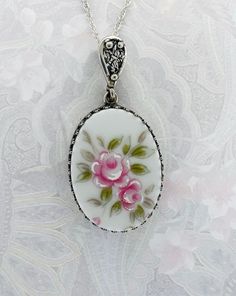 "This sterling silver heirloom pendant features a lovely spray of delicate hand painted roses.  For sweetness, joy and happiness, give her a pink rose! The hand carved cabochon displays white highlighted pale pink roses and soft green foliage nestled in a sterling silver crown setting.  Handmade Broken China Pendant *Carefully hand cut and shaped from a vintage china dish *Size: oval (approx.).75 inch x 1.1 inch *Materials: ceramic, sterling silver bezel,           bail, and rope chain (16/18/20/24\")            epoxy resin *Upcycled *'Very Vintage' Victorian Style Jewelry * I very carefully choose a china pattern that is appealing to the eye and hand shape the cabochon to fit the setting. No two pieces are ever exactly the same. Please expect small surface and edge imperfections due to th Enameled Jewelry, Victorian Style Jewelry, Mothers Day Present, Pale Pink Roses, Broken China Jewelry, Painted Roses, Sweet Necklace, Hand Painted Roses, Floral Jewelry