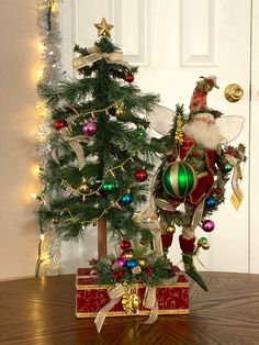 a small christmas tree sitting on top of a wooden table next to a santa clause figurine