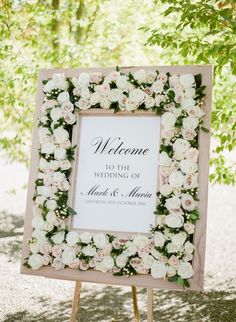 a welcome sign with white flowers on it and a wooden easer underneath the sign