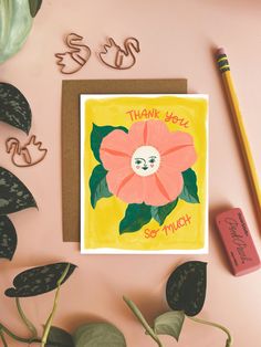 a card with a pink flower on it next to some green leaves and pencils