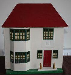 a white doll house with red roof and green shutters on the front, sitting on a table