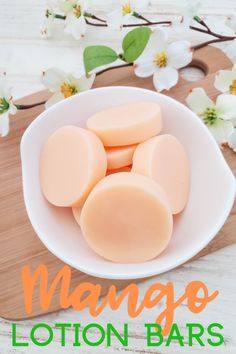 mango lotion bars in a white bowl on a wooden cutting board with flowers behind it