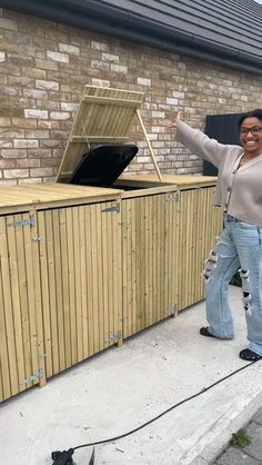 a woman standing next to a large wooden chest on the side of a road in front of a brick building