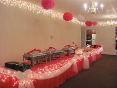 a banquet hall with red and white table cloths, silver buffet tables and pink tissue pom poms