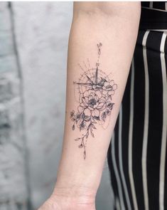 a woman's arm with a compass and flowers tattoo on the left inner arm