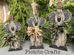 three wooden mice with bows on their heads are sitting in front of some greenery