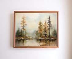 a painting hanging on the wall next to a white wall with a brown frame and some trees