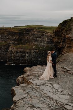 a bride and groom standing on the edge of a cliff