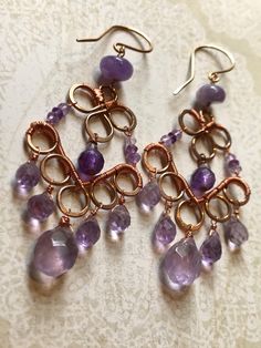 two pairs of earrings with purple beads and wire work hanging from them on a lace doily